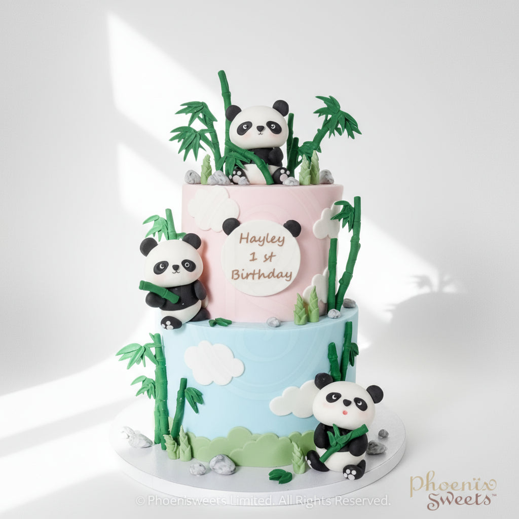 A two-tier fondant cake decorated with panda bears, bamboo, and clouds, with 'Happy 1st Birthday' message on the top tier.