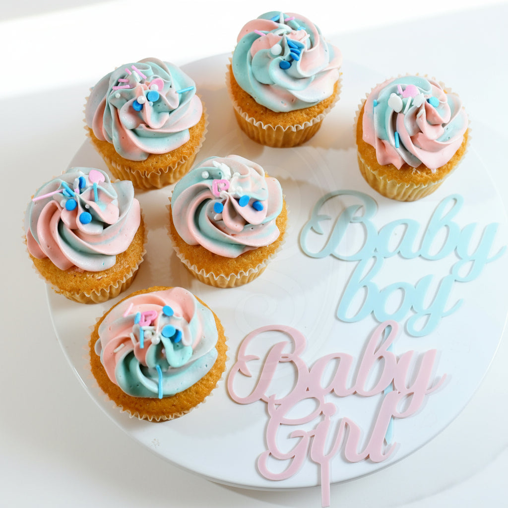 A set of decorated cupcakes on a plate with pastel blue and pink icing, presented on a plate with a 'Baby' sign in blue and pink.